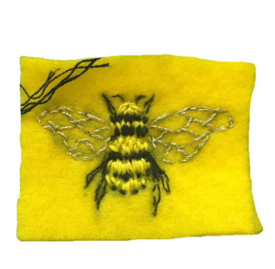 A realistic embroidered bee on a small patch of yellow felt. The wings are sewn with silver metallic thread.