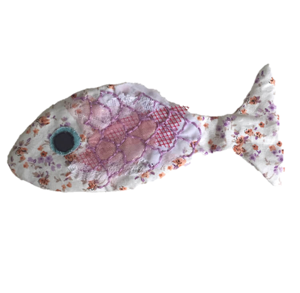 A hand-sewn fish made of lightly stuffed white and pink floral fabric, on which purple scales are embroidered over scraps of lace and netting.